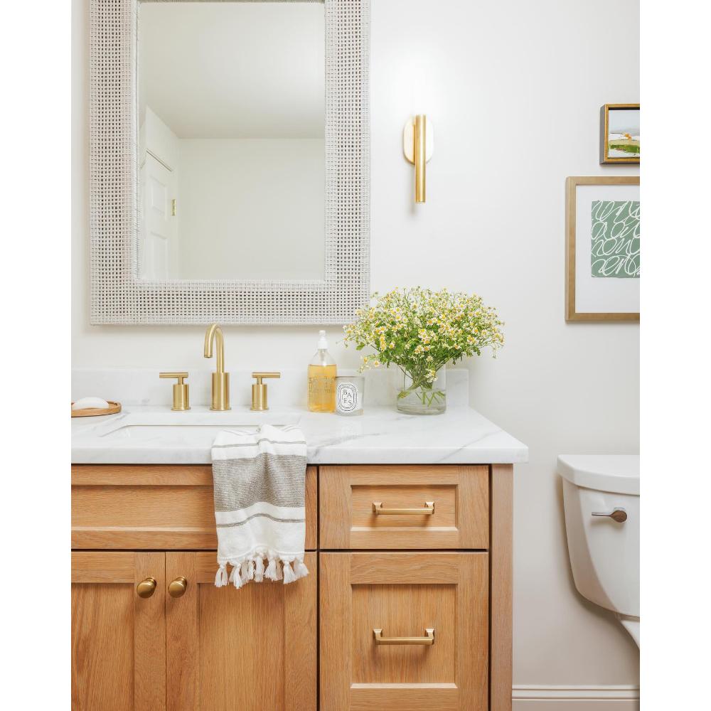 Bathroom with light wood vanity, marble top, gold fixtures, and a Made Goods Isla French Gray Peeled Rattan Mirror.