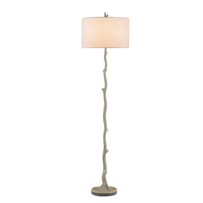 A floor lamp with a branch-like sculptural base in a distressed gray finish and a tapered drum shade in a warm beige fabric, shown against a plain white background.