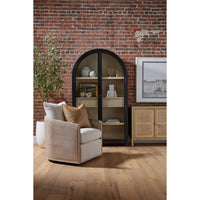 Beige armchair with pillows in a room with a brick wall and bookshelf.