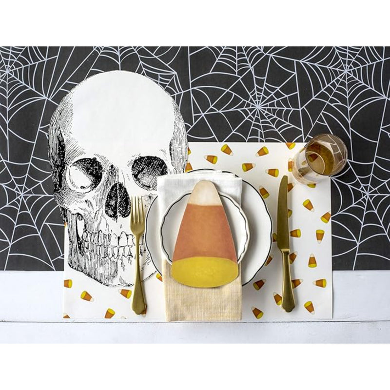 Create the perfect spooky tablescape for your Halloween party with a Halloween-themed table setting featuring a large skull print, candy corn decorations, and utensils placed on a Hester & Cook Halloween Spiderweb Paper Table Runner.