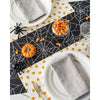 A spooky tablescape featuring the Hester & Cook Halloween Spiderweb Paper Table Runner, candy corn, a small pumpkin, and gray napkins on plates brings the perfect eerie charm to your Halloween party.