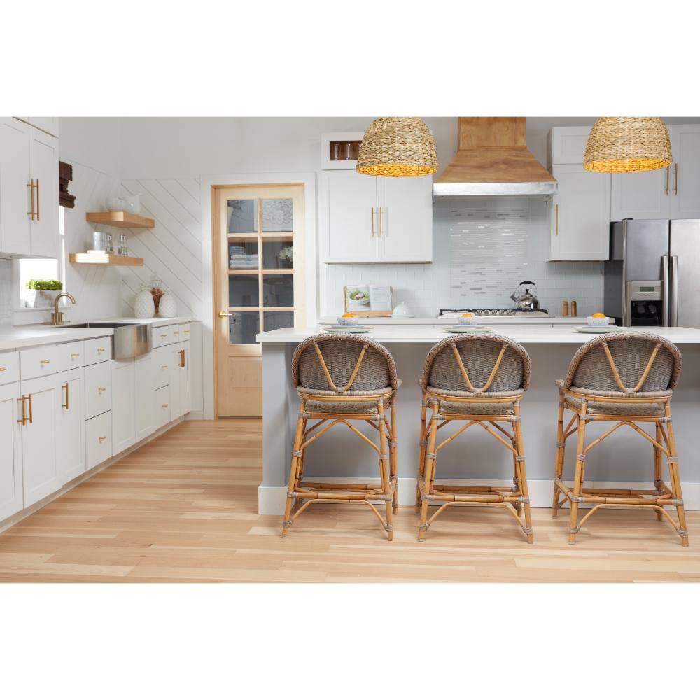 A bright modern kitchen with white cabinets, light wood flooring, a central island, and three woven wicker bar stools in front of the island. Two woven pendant lights hang above the counter.