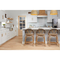 A bright modern kitchen with white cabinets, light wood flooring, a central island, and three woven wicker bar stools in front of the island. Two woven pendant lights hang above the counter.