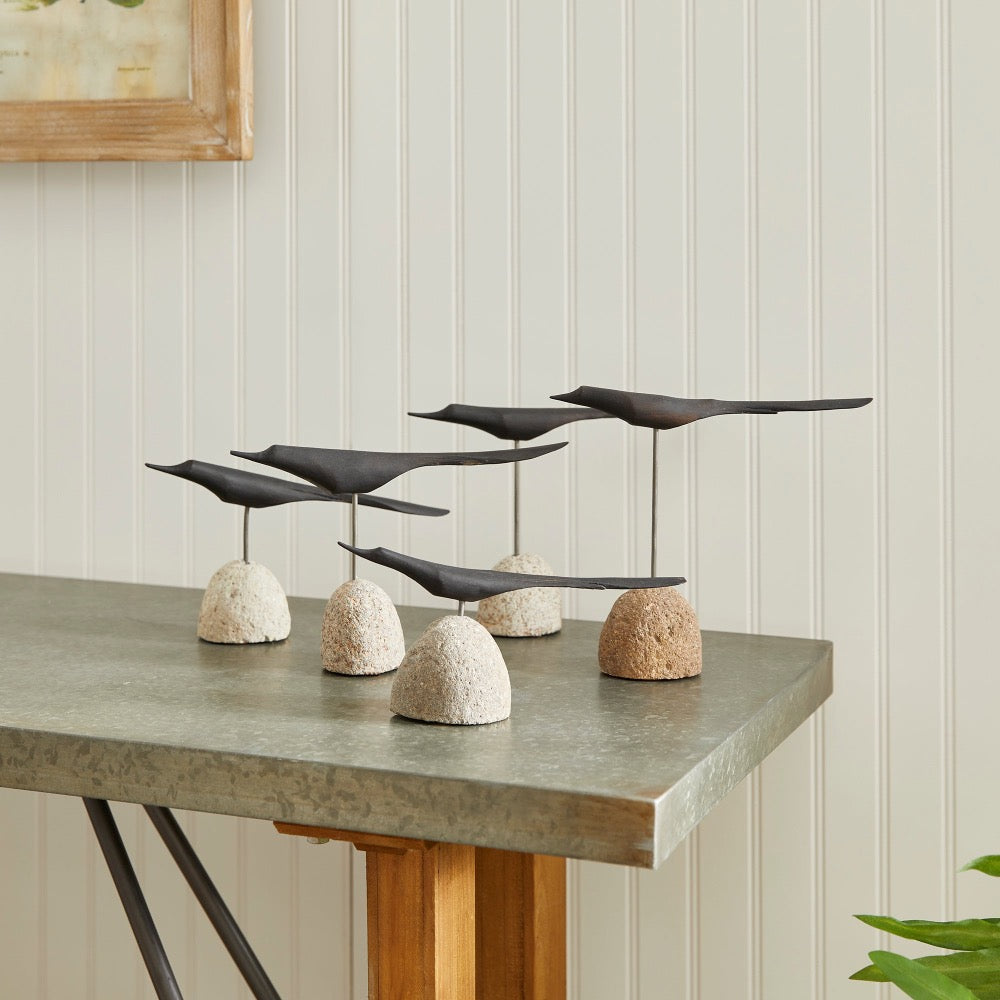 Decorative sculpture of black birds on stone bases on a table against a light wall.
