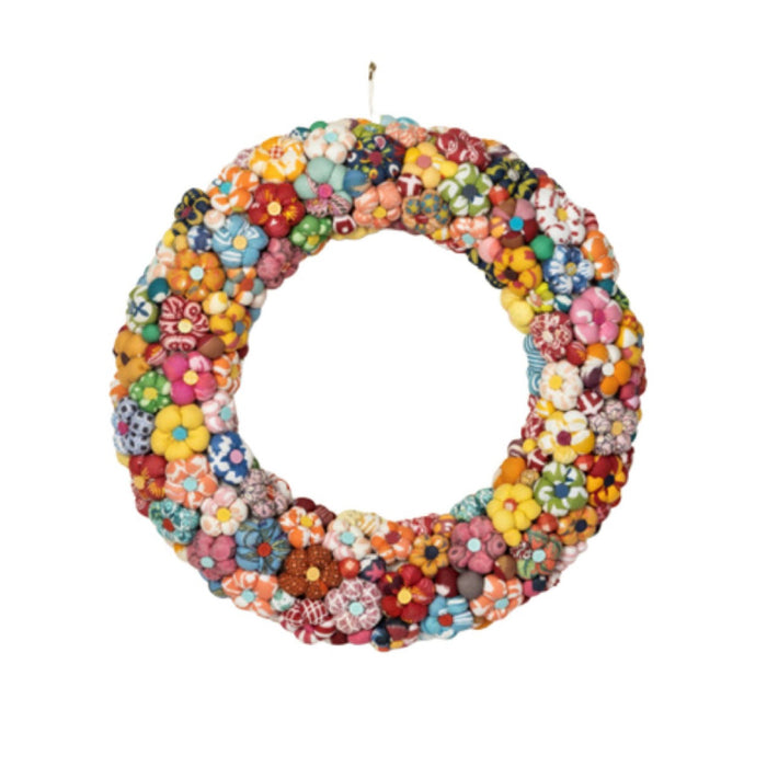 A circular fabric flower wreath made of many colorful sewn fabric flowers in assorted patterns and hues, hanging against a plain white background.