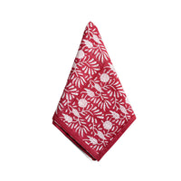 A folded red cloth napkin with a white floral and leaf pattern, displayed on a clean white background.