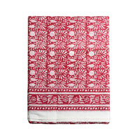 A folded red fabric tablecloth, featuring a white block-print style floral and leaf pattern with a decorative border at the bottom, shown against a plain white background.