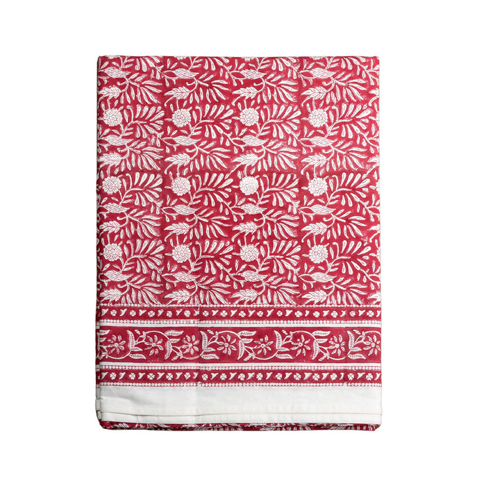 A folded red fabric tablecloth, featuring a white block-print style floral and leaf pattern with a decorative border at the bottom, shown against a plain white background.