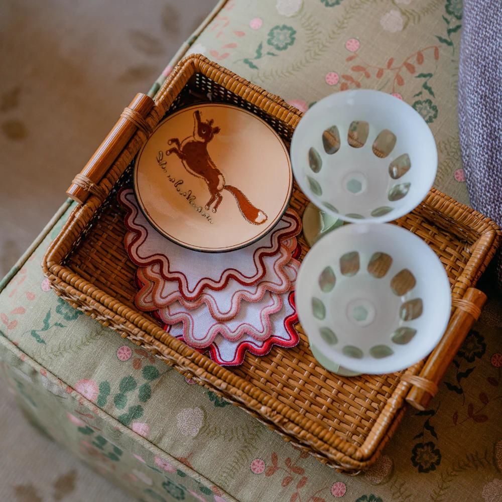 Decorative items including a plate with a fox design, a white martini glasses, and a rattan tray on a floral-patterned surface.