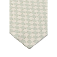 A close-up of a textured area rug with a woven checkerboard pattern in sage green and off-white, showing the corner and loop pile texture against a white background.