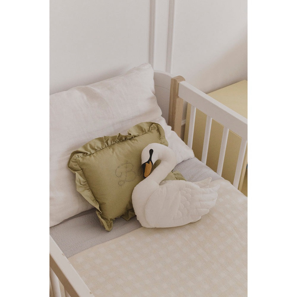 Crib with white swan plush toy and green pillow on a light background