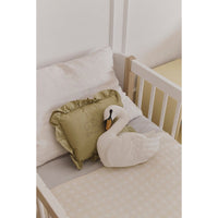 Crib with white swan plush toy and green pillow on a light background