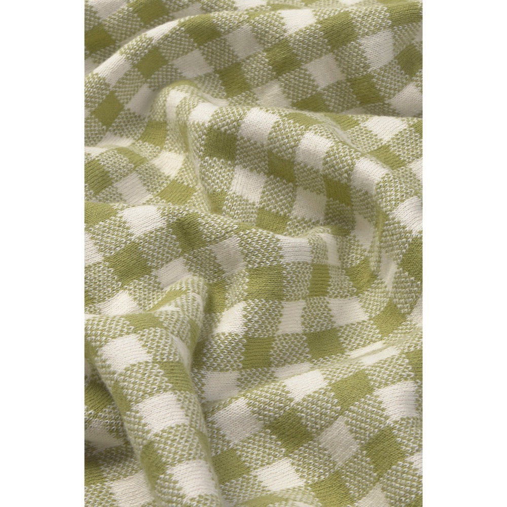 A close-up of a woven fabric with a green and off-white gingham check pattern, shown with soft folds and texture.