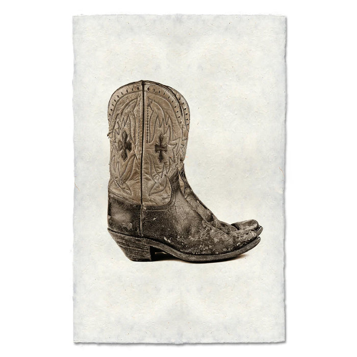 A rustic art print featuring a single distressed brown leather cowboy boot with western embroidery, centered on a textured off-white paper background.