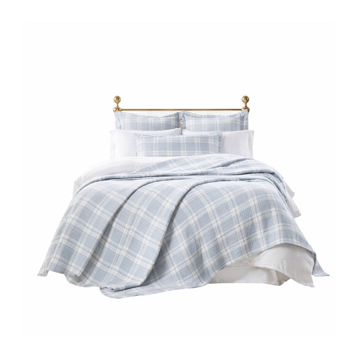 A bed with a brass headboard, white bedding, and Doyle Sky Bedding Collection by Orchids Lux Home in blue check.