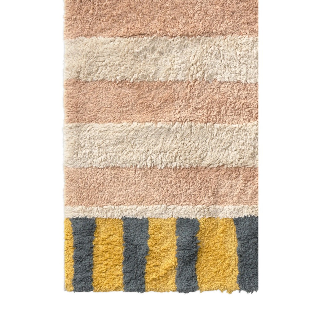 A close-up of a plush shag rug with horizontal stripes in dusty pink, cream, and mustard yellow with dark gray vertical stripes at the bottom.
