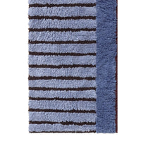 A close-up of a textured shag rug featuring horizontal stripes in light blue and dark brown, with a solid medium blue border on the right side.