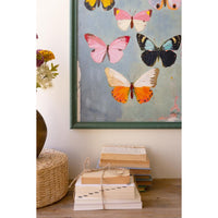 Framed artwork of butterflies on a wall above stacked books.