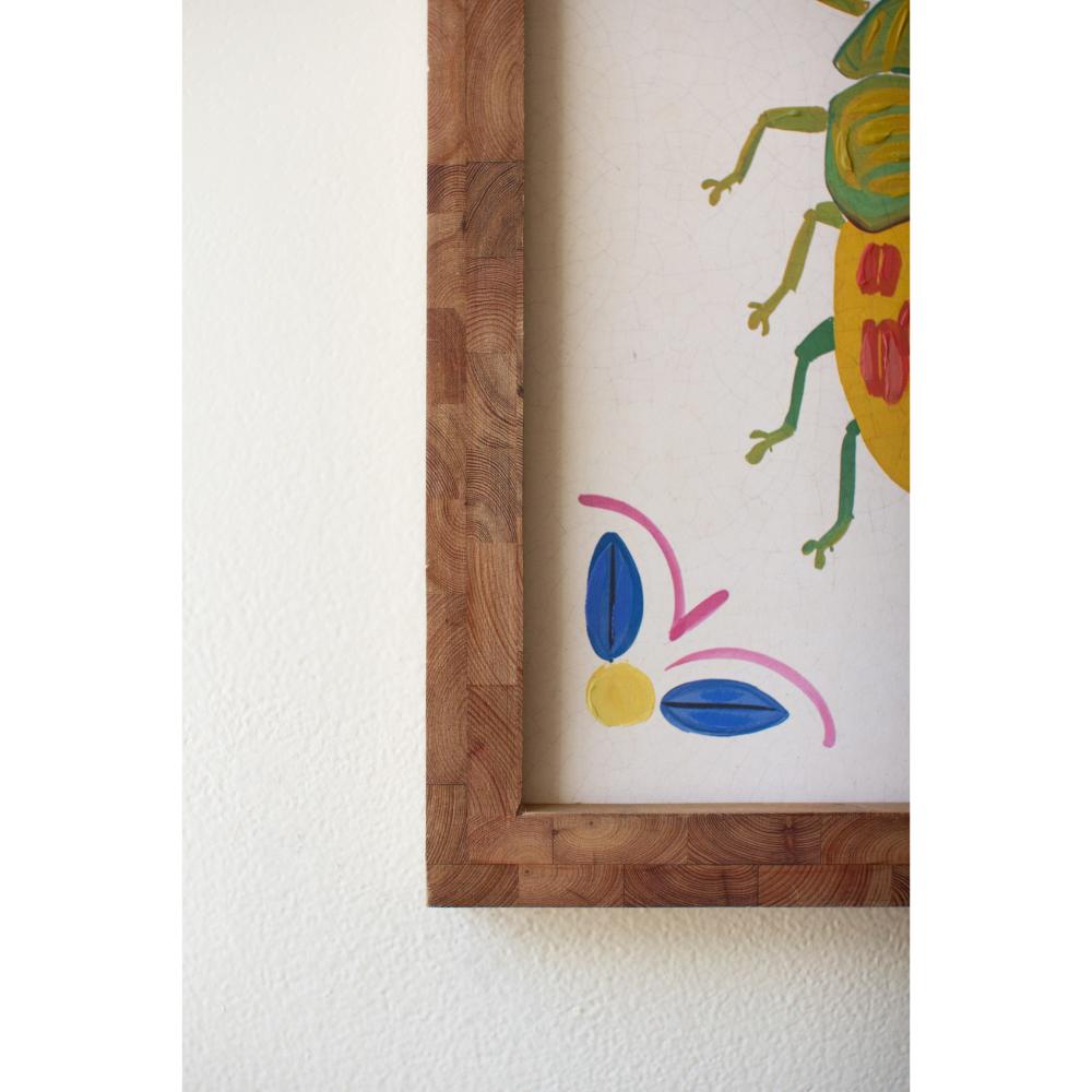 Colorful abstract drawing of a beetle in a wooden frame on a white wall.