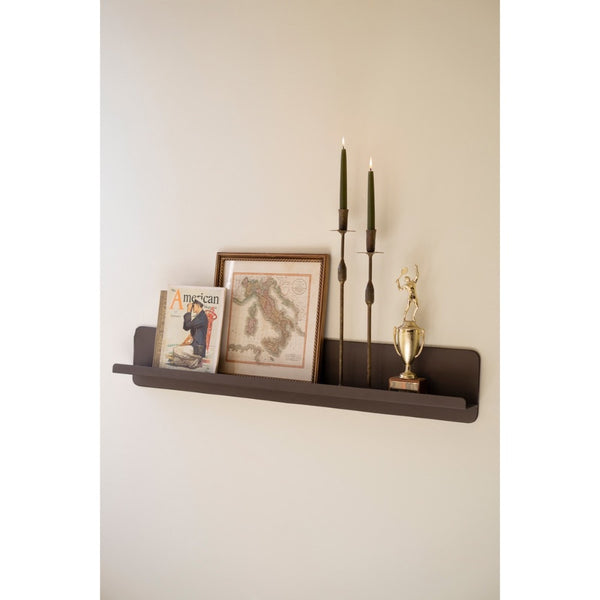 Wall-mounted shelf with decorative items including a magazine, framed picture, candles, and a trophy on a plain wall.