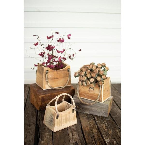 Three wooden baskets with floral arrangements on a rustic wooden surface.
