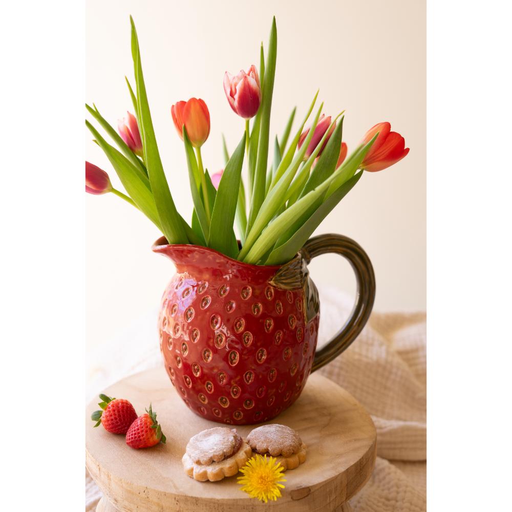 Red ceramic pitcher with tulips on a wooden surface
