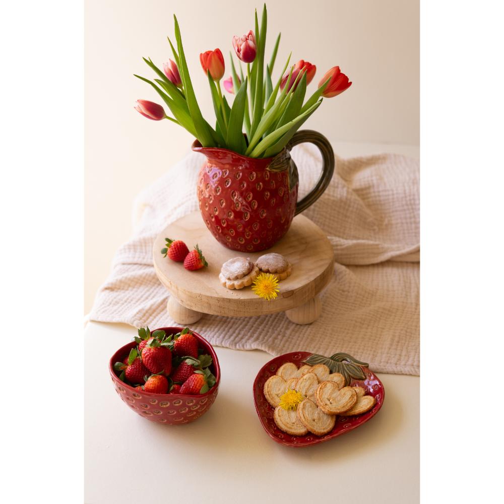 Red mug with tulips, bowl of strawberries, and plate of cookies on a light surface.