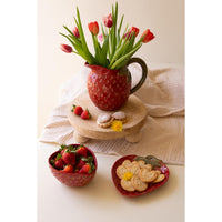 Red mug with tulips, bowl of strawberries, and plate of cookies on a light surface.