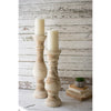 Two Kalalou Hand Carved Wooden Candle Stands with white candles complement books and a small plant on a rustic surface.