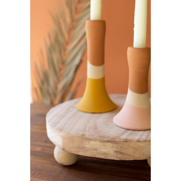 Two colorful ceramic candle holders with candles on a wooden surface against an orange wall.