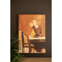 A framed still life painting hanging on a dark brown wall, showing a yellow vase with white flowers on a table, alongside a chair, wine glass, and bottle. A green potted plant sits at the bottom left.