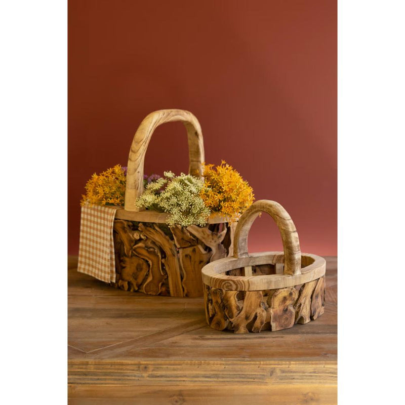 Two Kalalou Driftwood Baskets with Handles filled with flowers on a wooden surface against a rust backdrop.