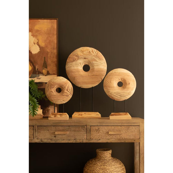Three round wooden wall art pieces with natural grain patterns displayed on black metal stands on a rustic wooden console table against a dark brown wall.