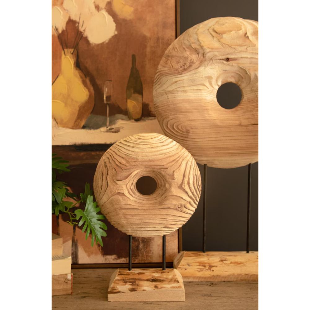 Two round wooden wall art pieces with circular cutouts, displayed on black metal stands against an indoor rustic wall backdrop.