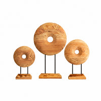 Three rustic wooden donut-shaped decorative sculptures of different sizes, each mounted on a black metal stand with a rectangular wooden base, arranged against a plain white background.