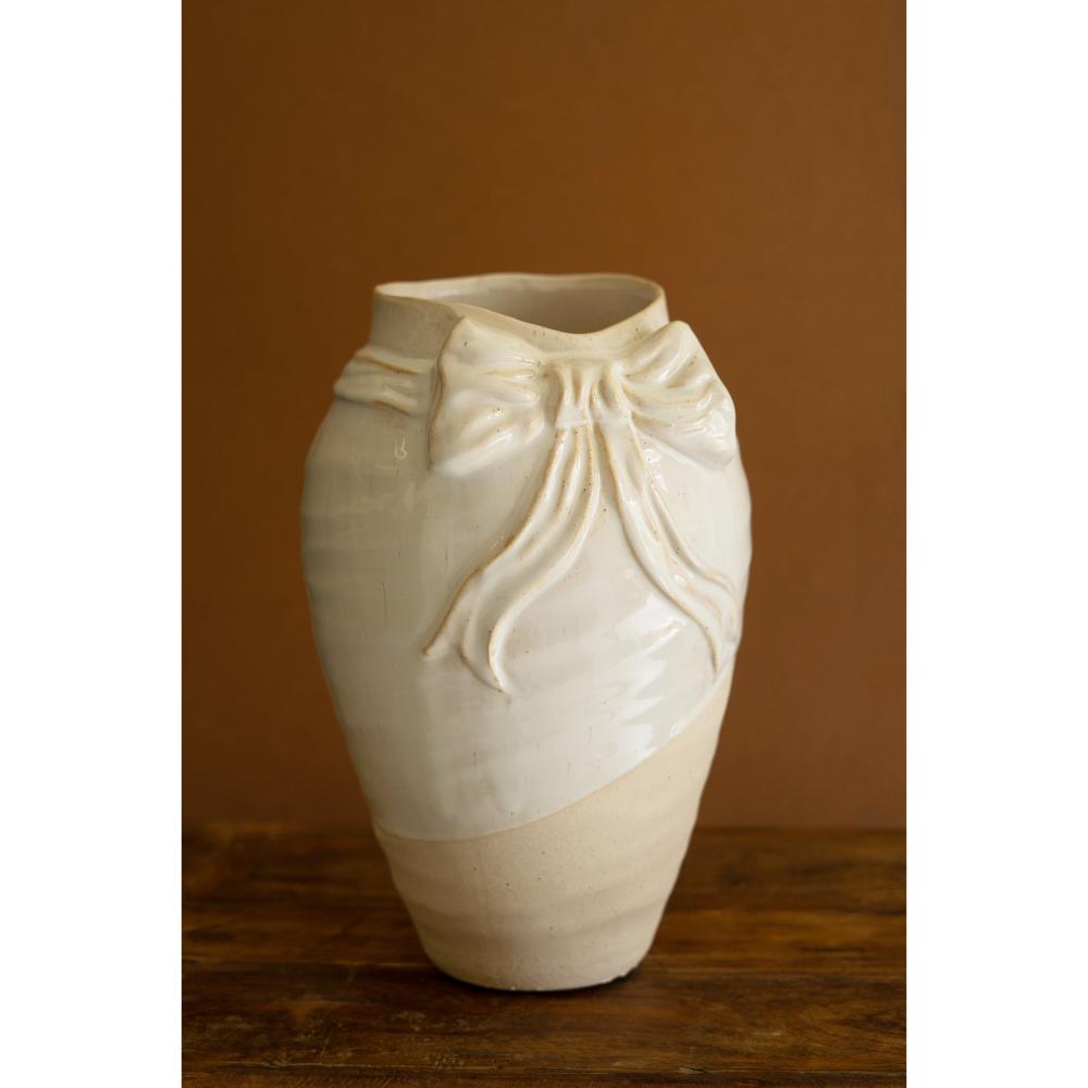 White ceramic vase with a decorative bow on a wooden surface and brown background