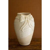 White ceramic vase with a decorative bow on a wooden surface and brown background