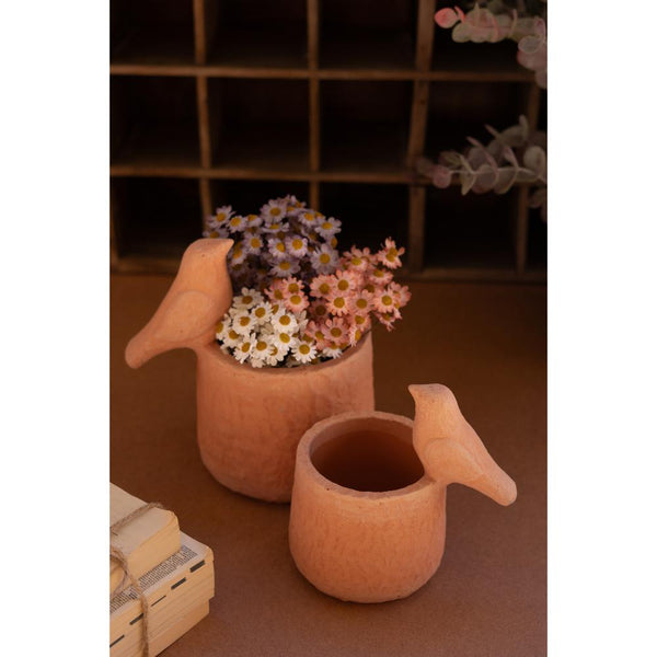 Two terracotta pots with floral arrangements on a wooden surface.