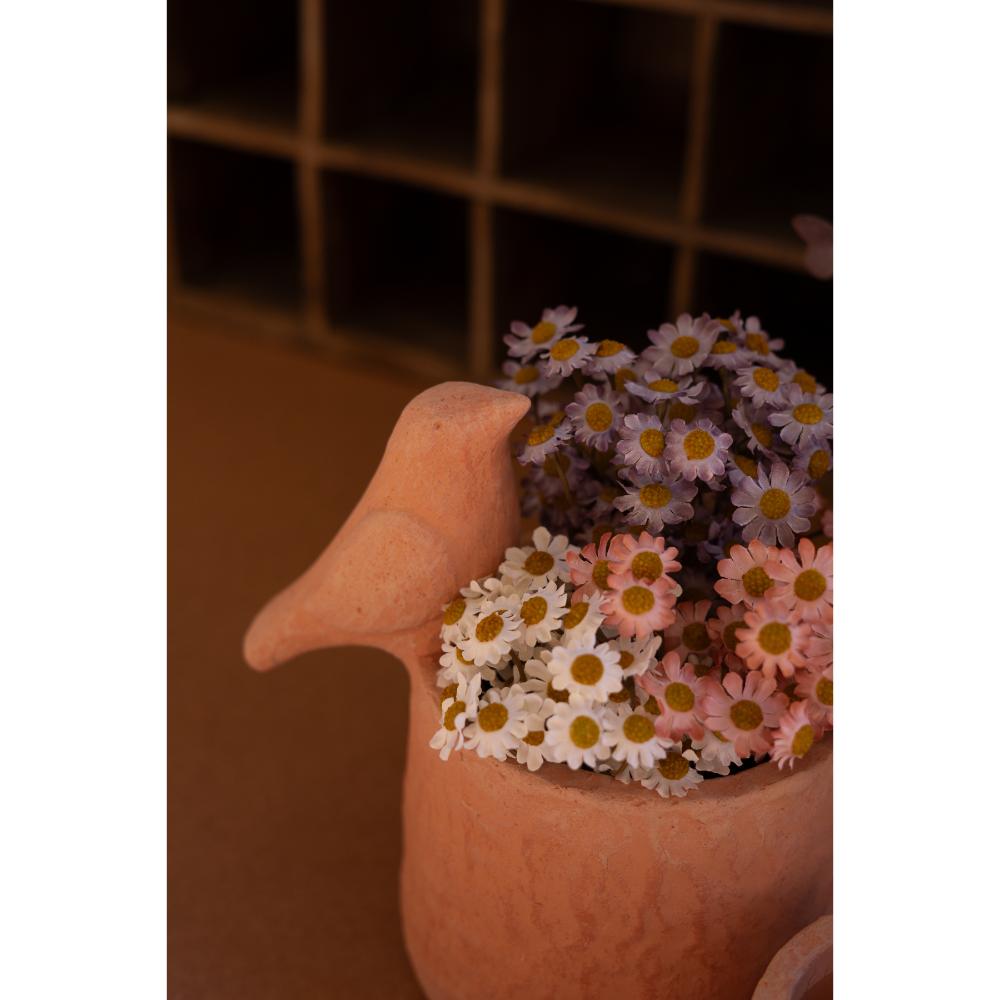 Ceramic bird with flowers in its beak against a dark tiled wall.