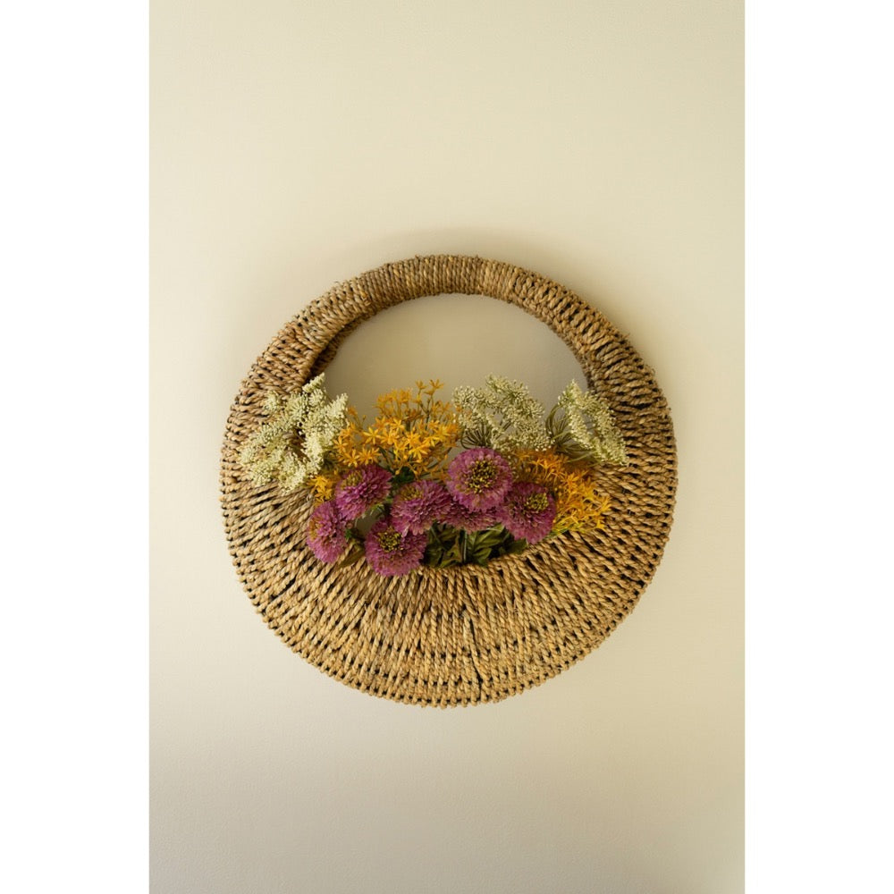 A Kalalou Woven Vine Wall Basket (set of 2) displays vibrant purple, yellow, and green flowers as natural decor.