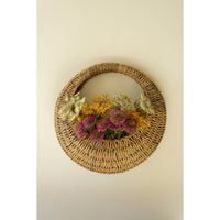 A Kalalou Woven Vine Wall Basket (set of 2) displays vibrant purple, yellow, and green flowers as natural decor.