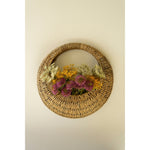 A Kalalou Woven Vine Wall Basket (set of 2) displays vibrant purple, yellow, and green flowers as natural decor.