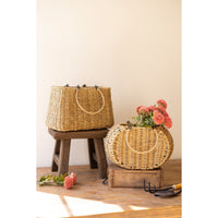 Wicker baskets with flowers on wooden stands against a beige wall.