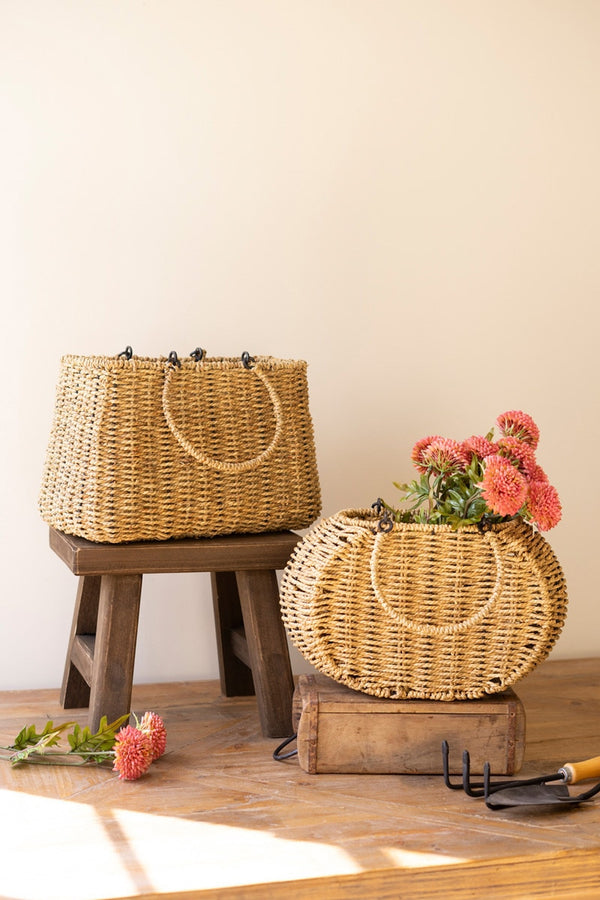 Wicker baskets with flowers on wooden stands against a beige wall.