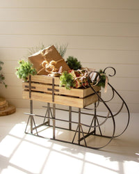 Wooden sleigh with Christmas decorations and presents on a white wooden floor.