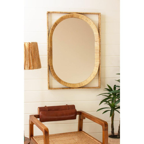 Rattan-framed mirror on a wall with a brown leather chair and plant in the foreground.