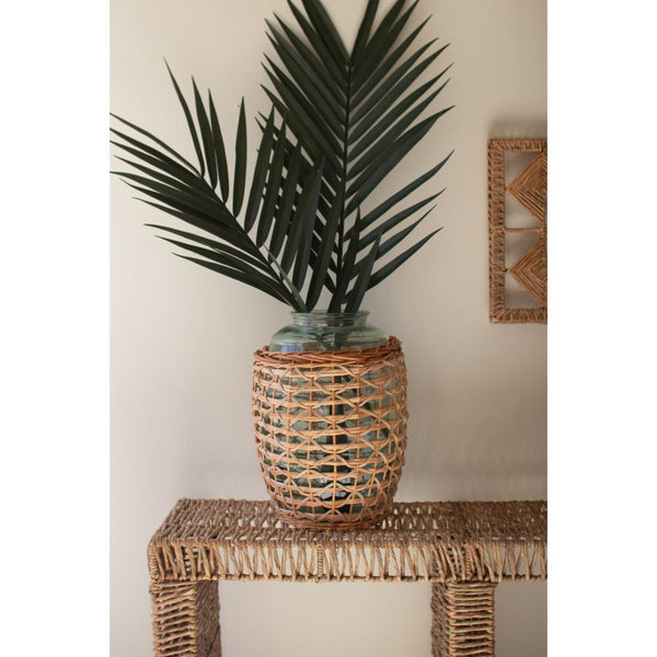Potted plant in a woven basket on a wicker table against a neutral wall.