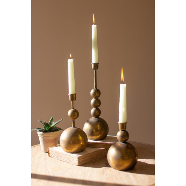 Decorative candle holders with candles on a wooden surface against a beige wall.