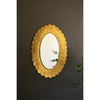 The Layered Gold Scallop Framed Mirror by Kalalou reflects plant leaves, adding chic decor to a dark wall.