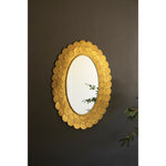 The Layered Gold Scallop Framed Mirror by Kalalou reflects plant leaves, adding chic decor to a dark wall.